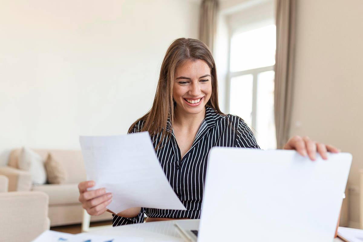 Käufer benötigt Dokumente für Immobilienkauf, Symbolfoto mit Frau am Notebook und Unterlagen in Hand
