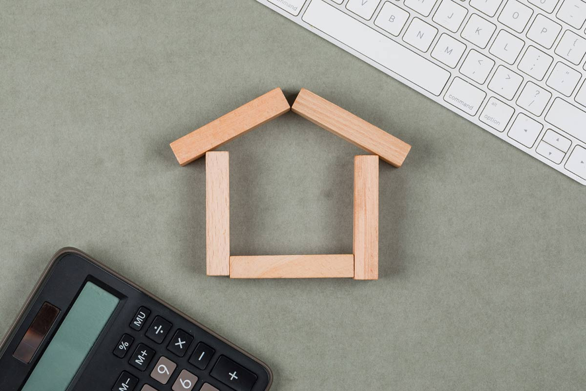 Symbolbild: Steuer sparen beim Immobilienverkauf mit Haus aus Holzstäben Taschenrechner