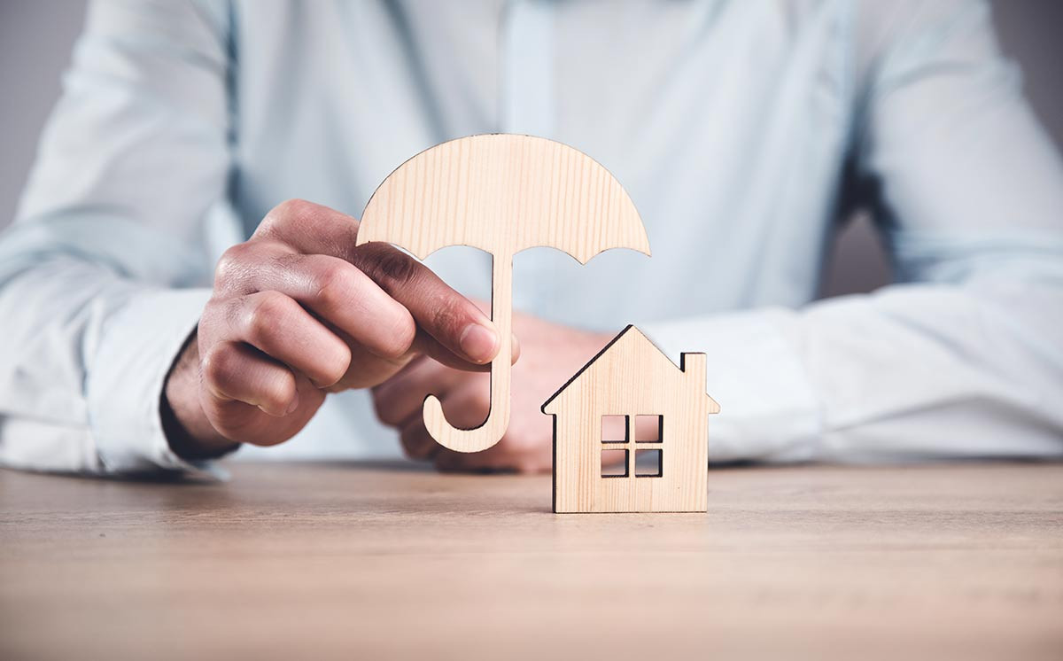 Mann hält Schutzschirm über Haus - Versicherungen sind wichtig