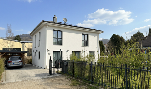 Modern single-family house with a photovoltaic system and a sunny garden, located in a quiet, slightly recessed position.