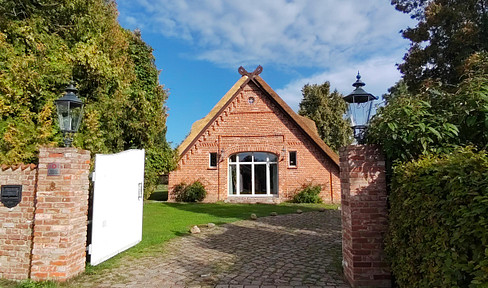 Completely renovated farmhouse with a thatched roof, situated on a natural plot of land on the edge of a field.